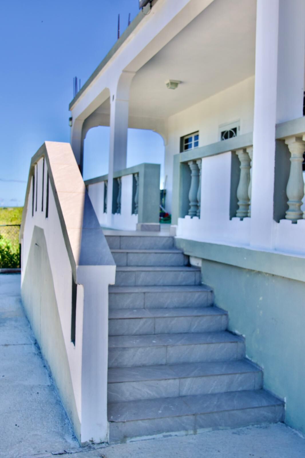 Un escalier menant à un bâtiment à la façade blanche, doté d’un balcon orné de balustrades.