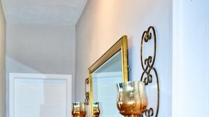 Un couloir avec une porte blanche, un miroir encadré d’or et deux appliques murales.