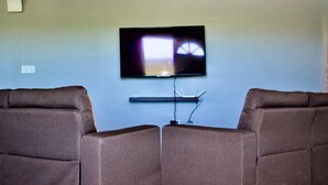 Een woonkamer met een flatscreen televisie aan de muur, aan weerszijden van twee bruine leren banken.