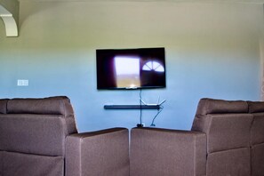 A living room with a flat-screen TV mounted on the wall, flanked by two brown leather sofas.