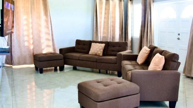 Un salon comprenant un canapé d’angle, deux fauteuils et un pouf assorti.