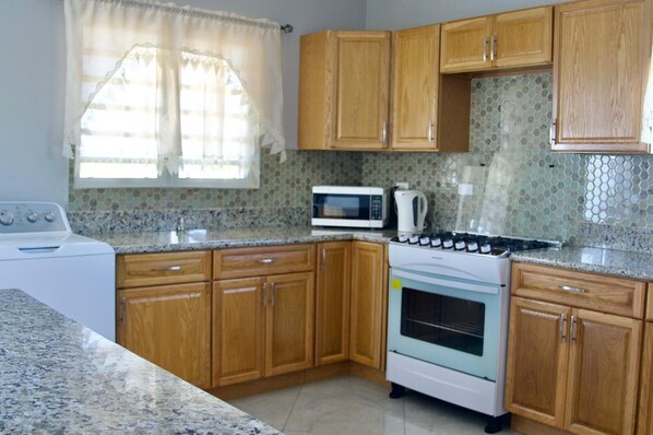 A kitchen with wooden cabinets, a stove, a microwave, and a window with curtains.