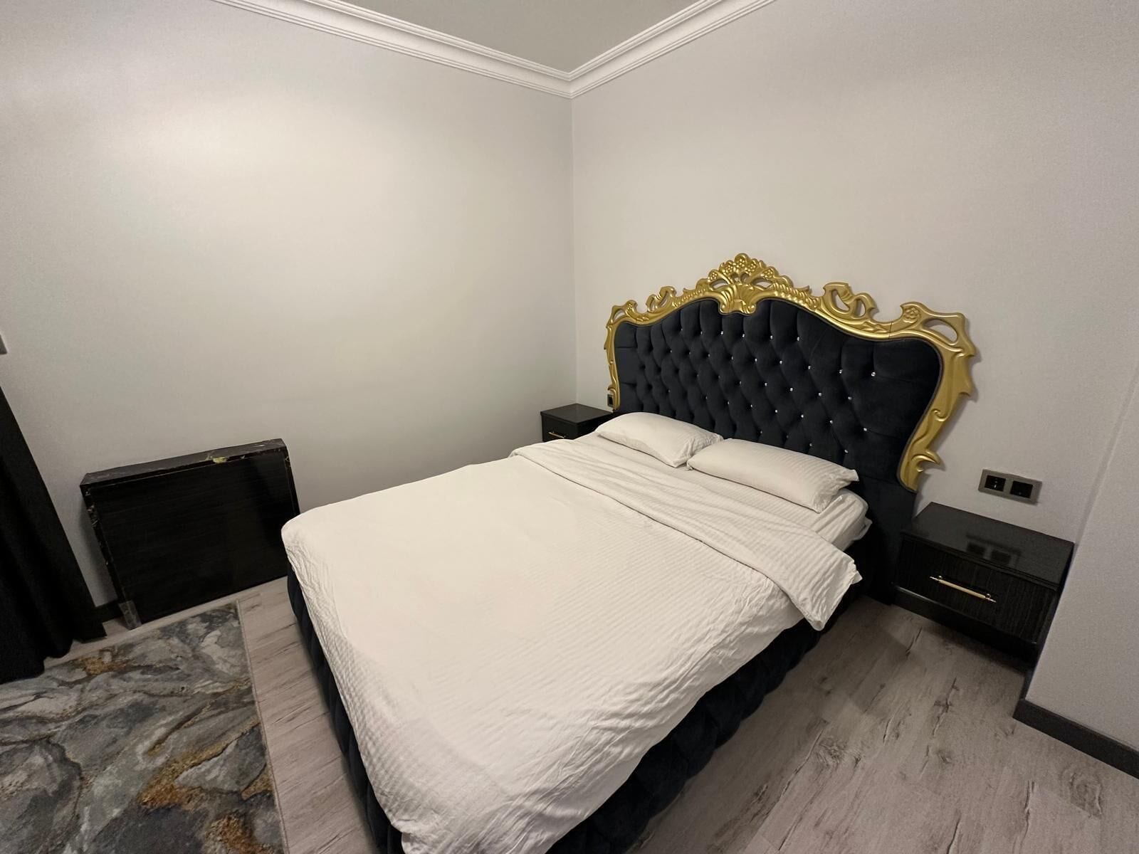 A bedroom with a large bed, a marble-patterned rug, and a classic black and gold headboard.