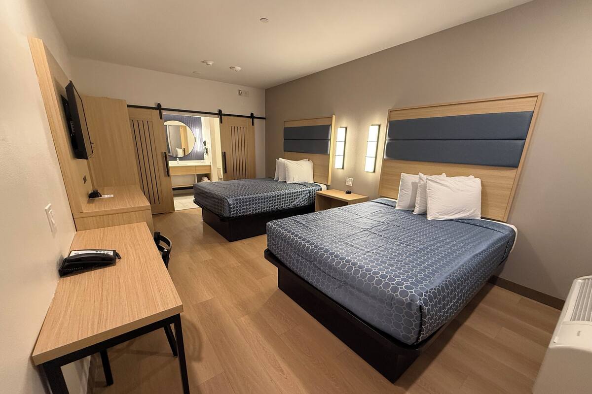 A hotel room with two beds, a desk, a mirror, and a TV.