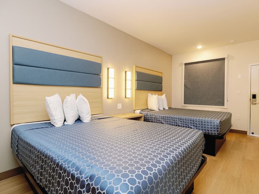 Quarto de hotel com duas camas, cada uma com cabeceira, mesa de cabeceira e luminária fixada na parede.