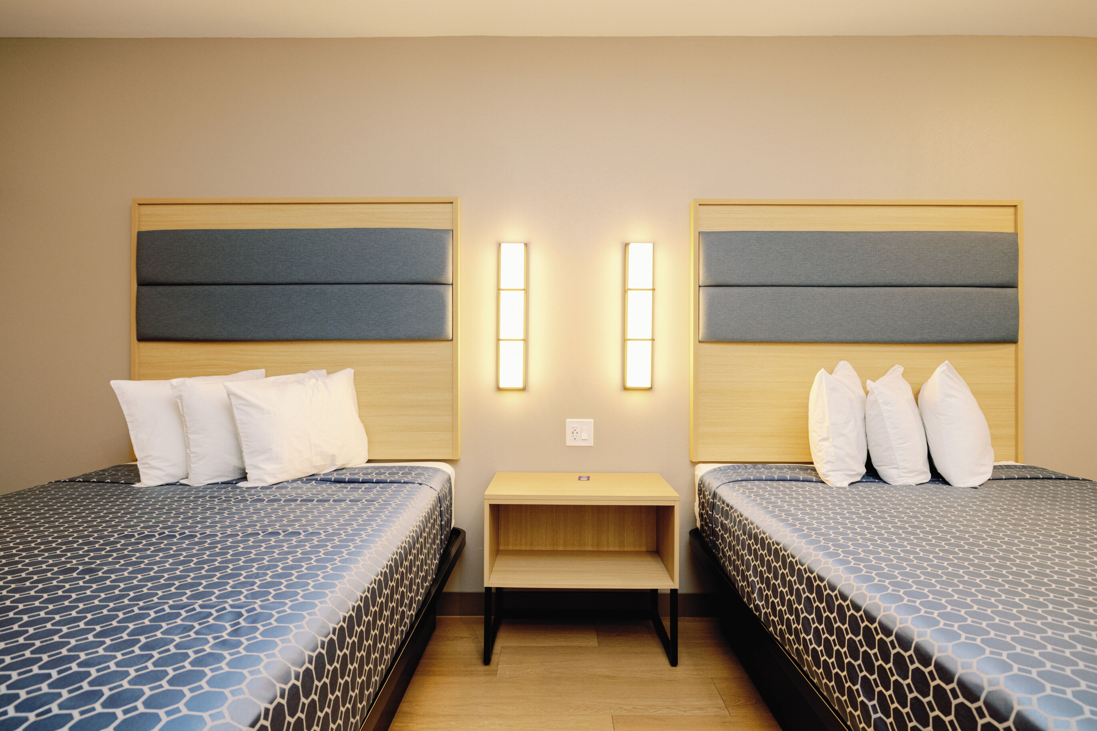 A hotel room with two beds, a nightstand, and a wall-mounted light fixture.