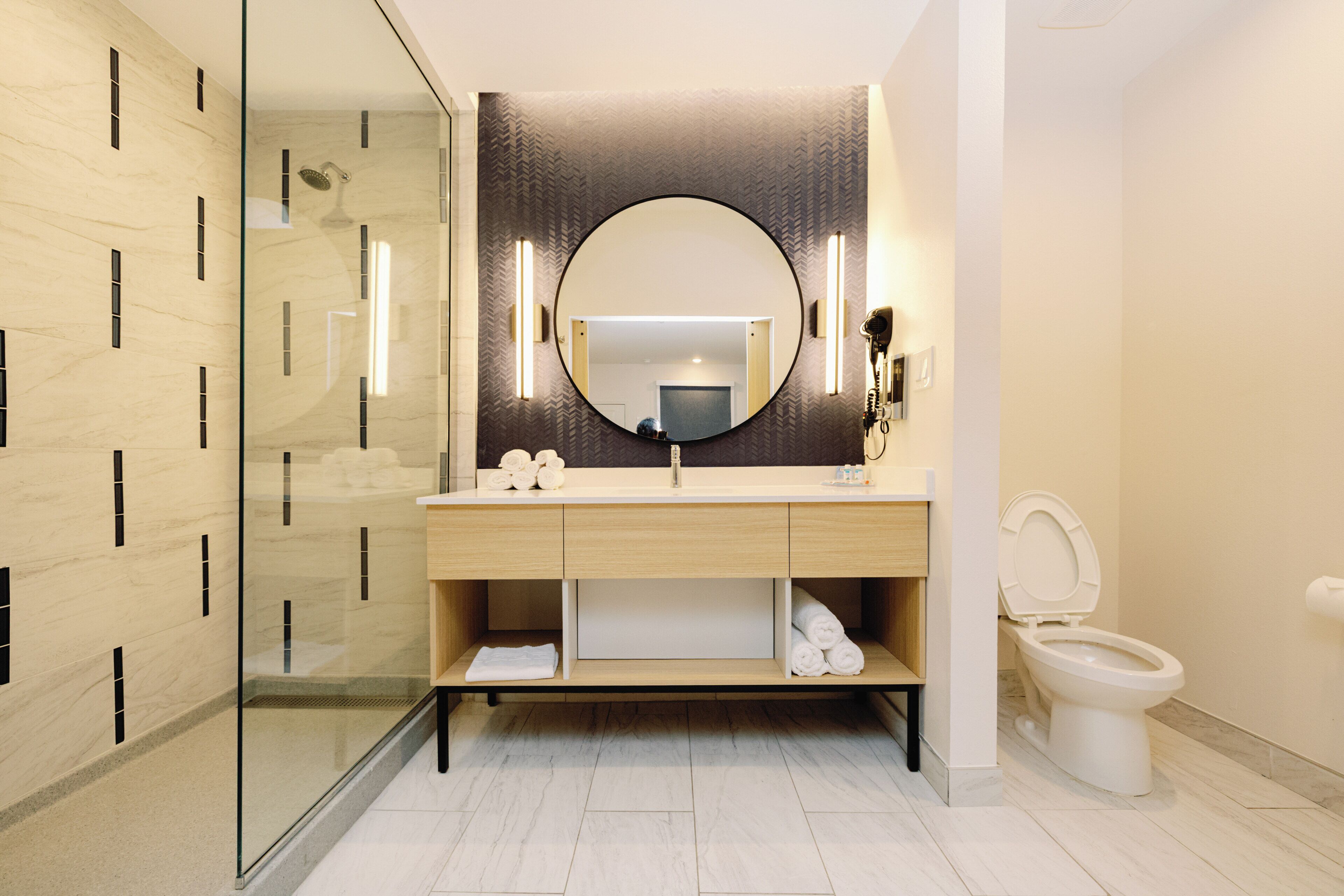 A modern bathroom with a glass shower enclosure, a round mirror, and a toilet.