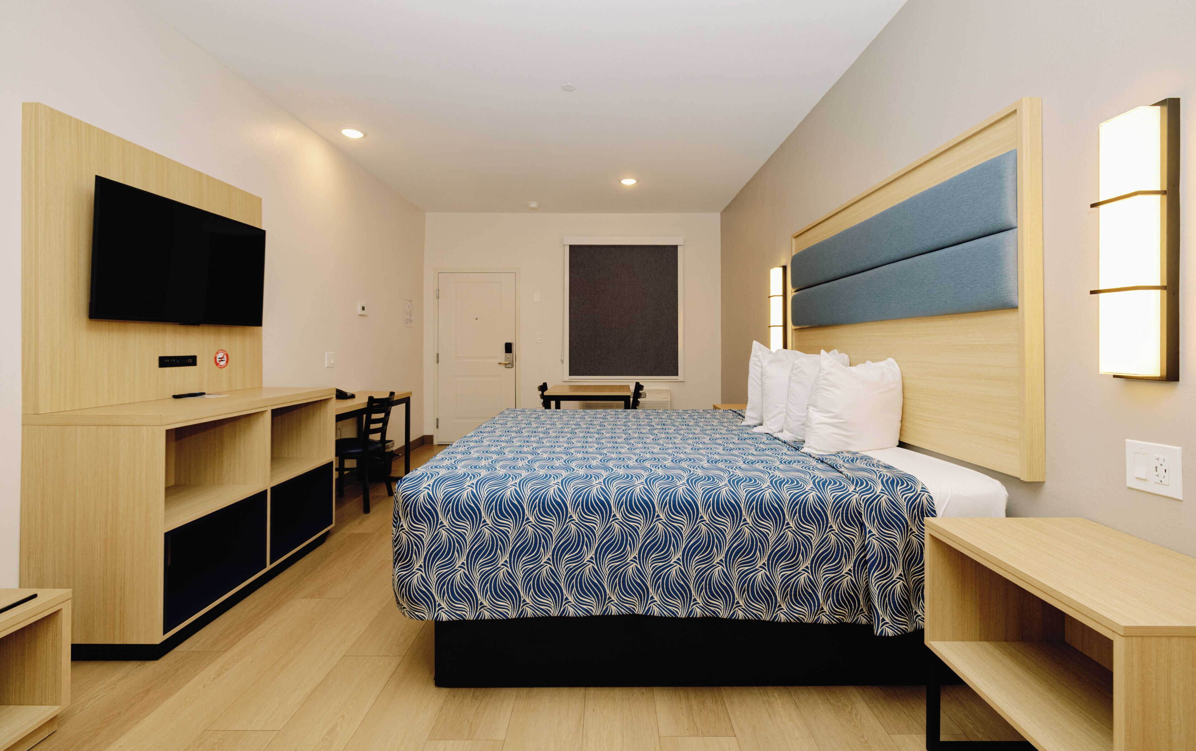 Habitación de hotel con cama, escritorio, silla, televisor y ventana grande.