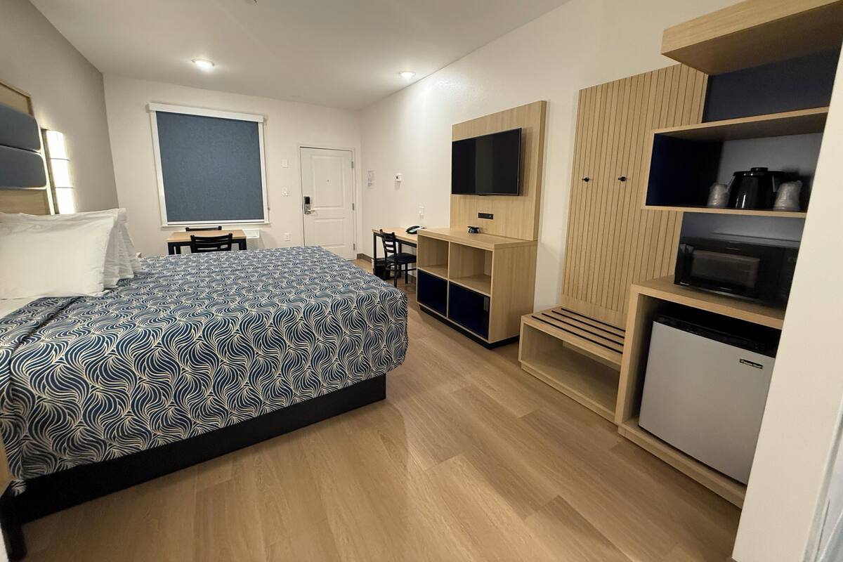 A modern hotel room with a large bed, a desk, a TV, and built-in storage.
