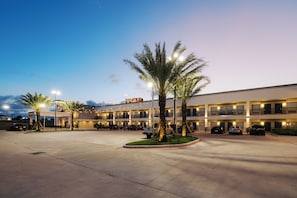 A multi-story hotel with a parking lot, palm trees, and string lights.