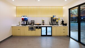 A modern hotel reception area with a clean, minimalist design, featuring a reception desk, a coffee machine, a refrigerator, and a glass door leading outside. - Palace Inn Blue 290 W 43rd & Bingle Rd (Houston)