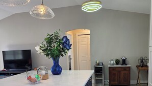 A modern kitchen with a marble countertop, dark cabinets, and gold handles. There is a large island with a vase of flowers, a coffee maker, and a TV on the left. - Cozy 2-bedroom house in The Villages Close To Golfing (Lady Lake)