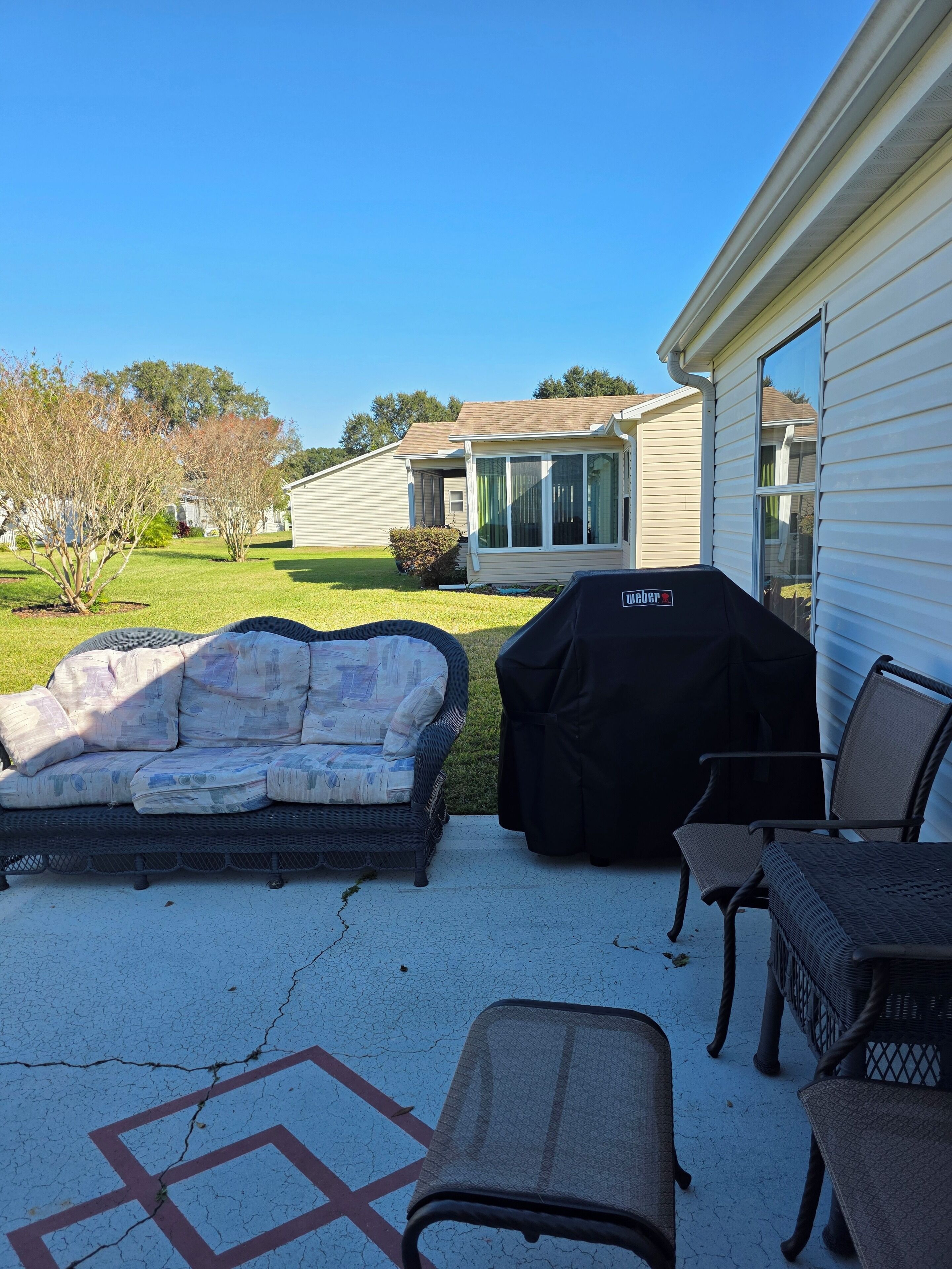 A patio with outdoor furniture, a grill, and a house in the background.