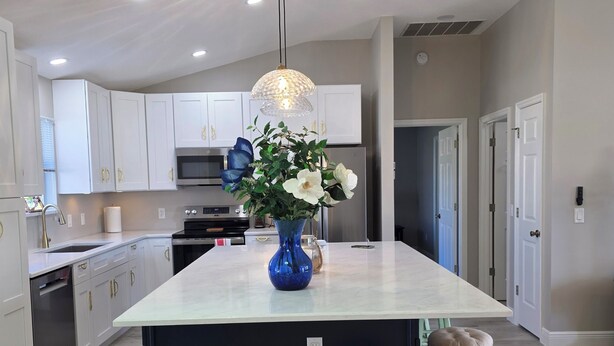 A modern kitchen with white cabinets, a central island, and a blue vase with flowers. - Cozy 2-bedroom house in The Villages Close To Golfing (Lady Lake)
