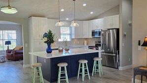 A modern kitchen with a central island, bar stools, stainless steel appliances, pendant lighting, and a ceiling fan. - Cozy 2-bedroom house in The Villages Close To Golfing (Lady Lake)