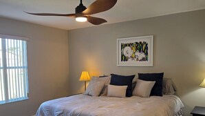 A bedroom with a bed, ceiling fan, artwork, and two bedside lamps. - Cozy 2-bedroom house in The Villages Close To Golfing (Lady Lake)