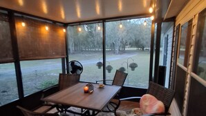 A covered patio with a table and chairs, large windows, and string lights.