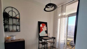 Un soggiorno moderno con un divano nero, un tavolo da pranzo con sedie, un tavolo consolle nero con oggetti decorativi, un lampadario a soffitto e un'ampia finestra con tende.