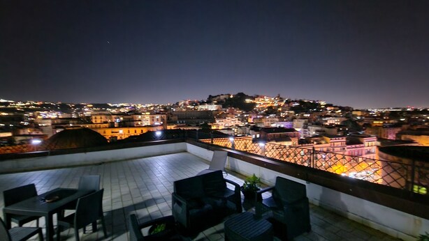 Una terrazza sul tetto con mobili da esterno e vista sulla città illuminata di notte.