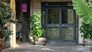 Ingresso di un edificio con una porta doppia scura, piante in vaso e un cartello visibile.