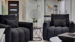 A modern living room with two grey armchairs, a small round table with a vase, and a wall-mounted flower decoration. - Houston white house, private pool, patio and game room the best place in Houston (Houston)
