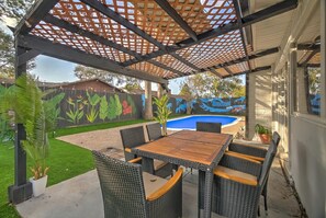 Eine überdachte Terrasse mit Pool, Gartenmöbeln und einem Wandgemälde.