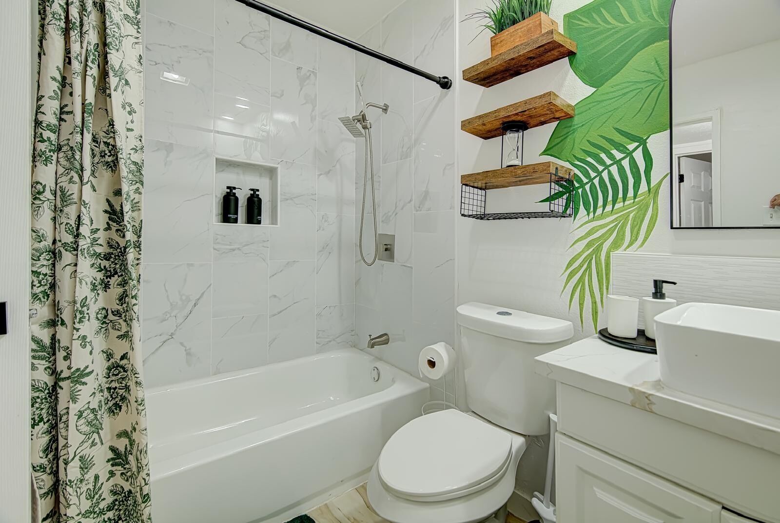 Une salle de bain moderne avec une baignoire, des toilettes et un lavabo. On y trouve des étagères en bois ornées de plantes et un grand miroir.