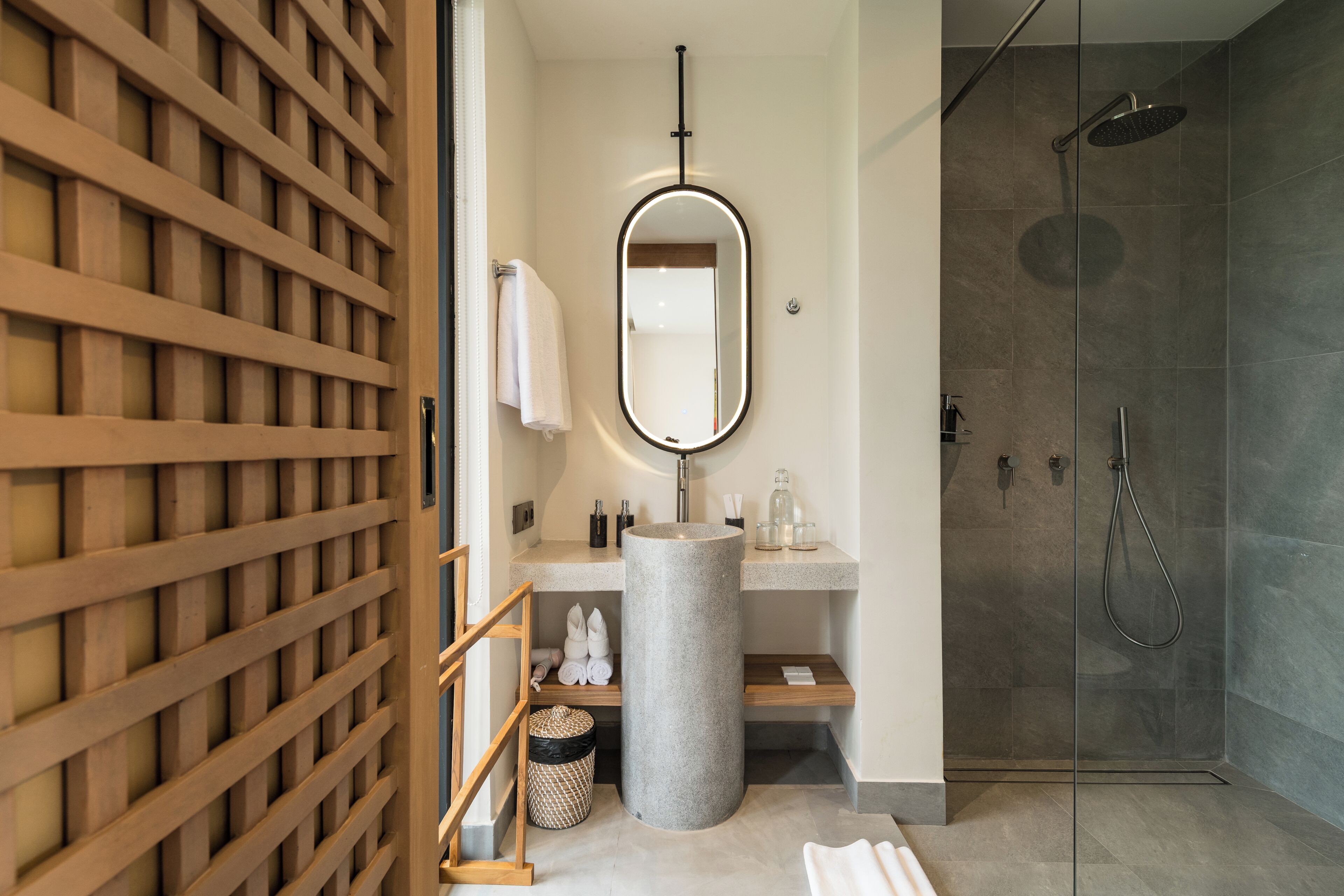 A modern bathroom with a freestanding mirror, a sink, a shower, and a wooden lattice partition.