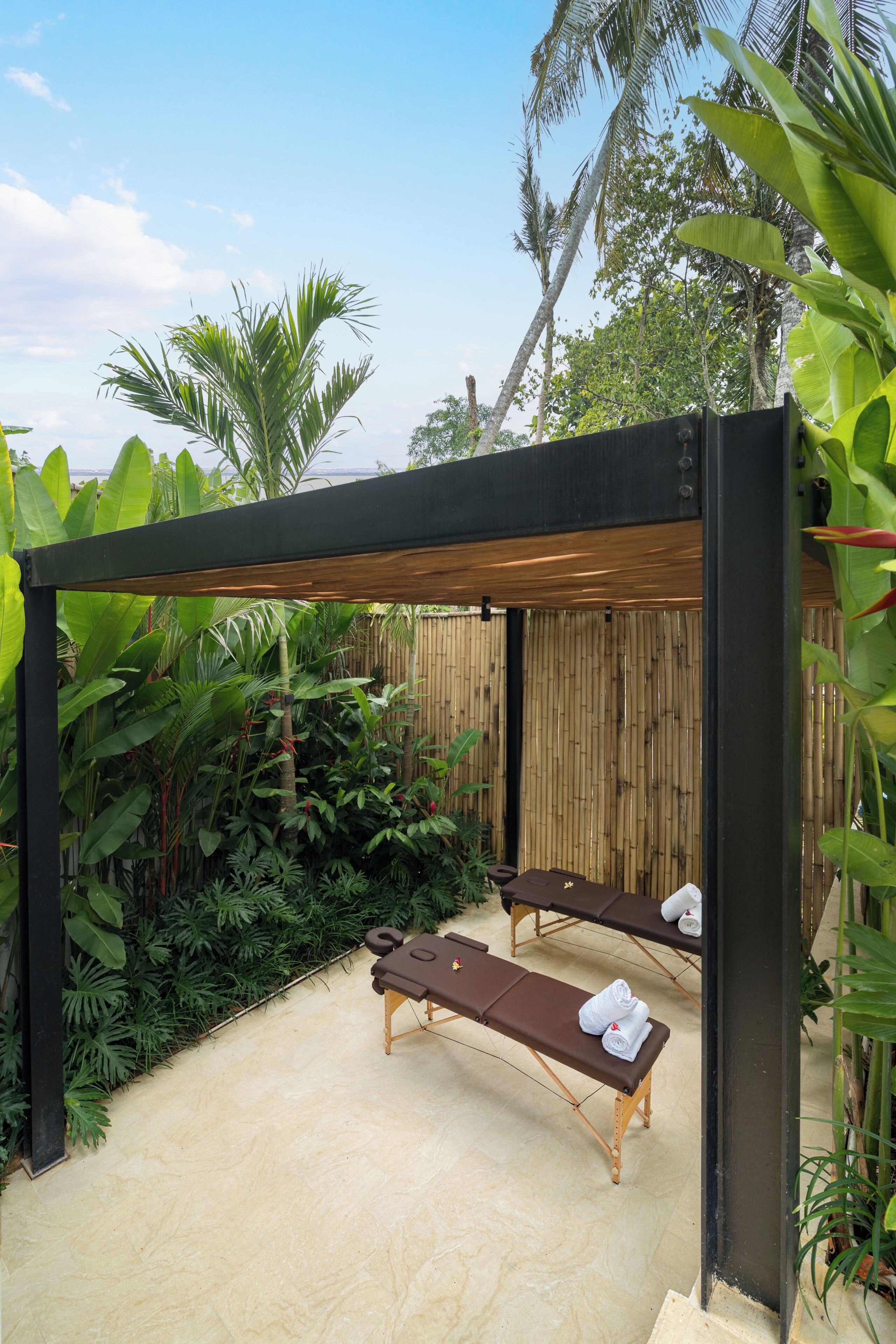 Un área de spa con dos camillas de masaje, una valla de bambú y abundante vegetación tropical.