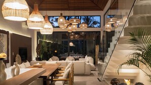 Un interior moderno con zona de comedor, sofás, lámparas colgantes de mimbre y una escalera.