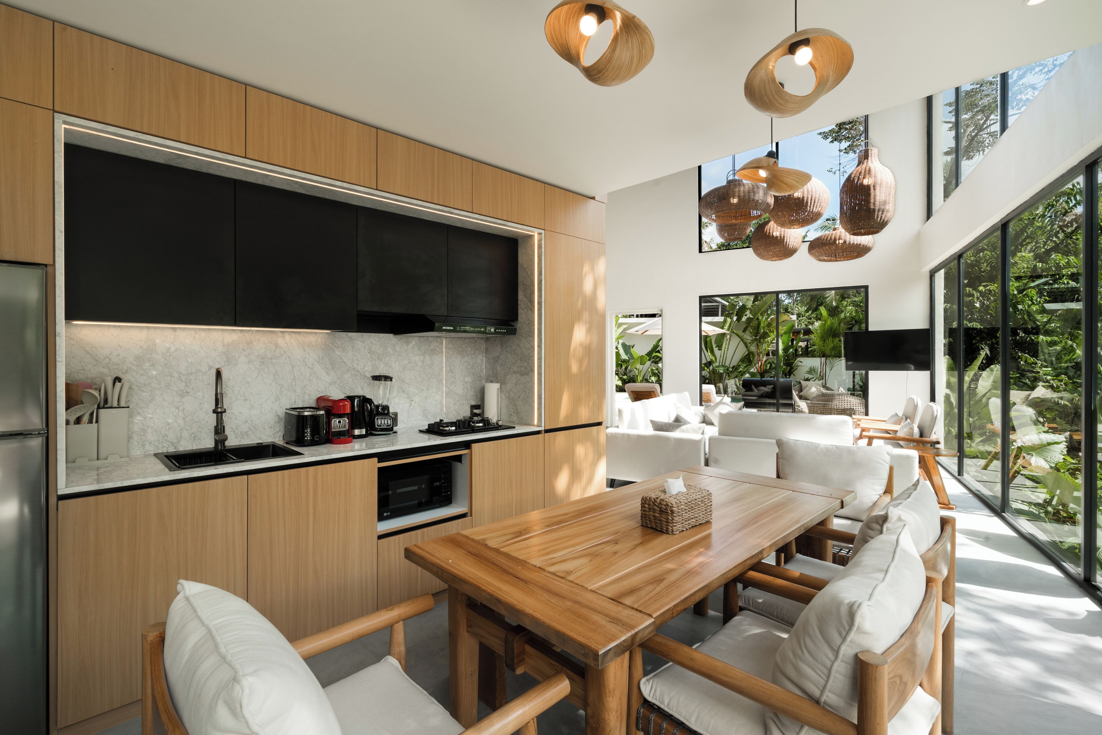 A modern kitchen with wooden cabinets, a large black TV, and a dining area with a wooden table and white chairs.