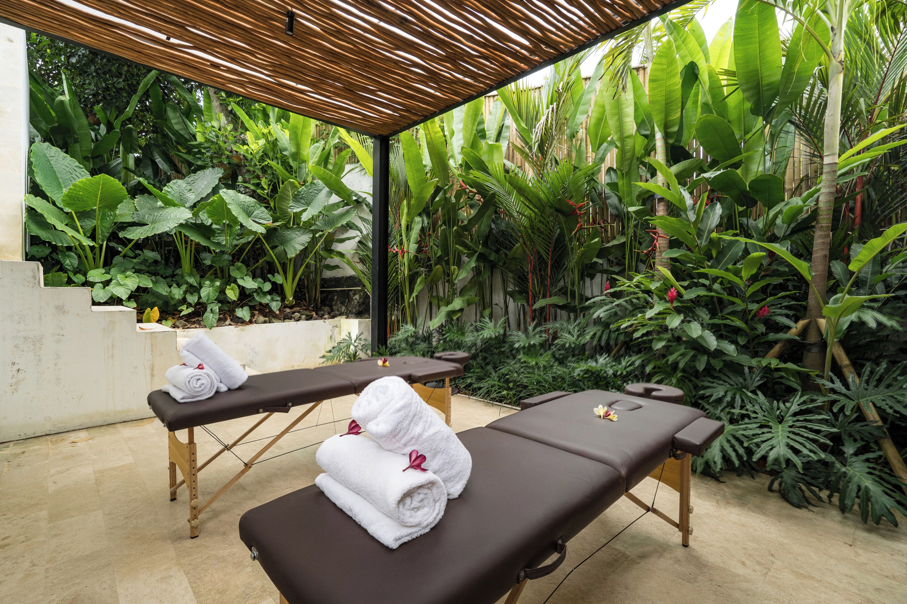 Un área de spa con dos camillas de masaje, techo de madera y exuberante vegetación tropical.