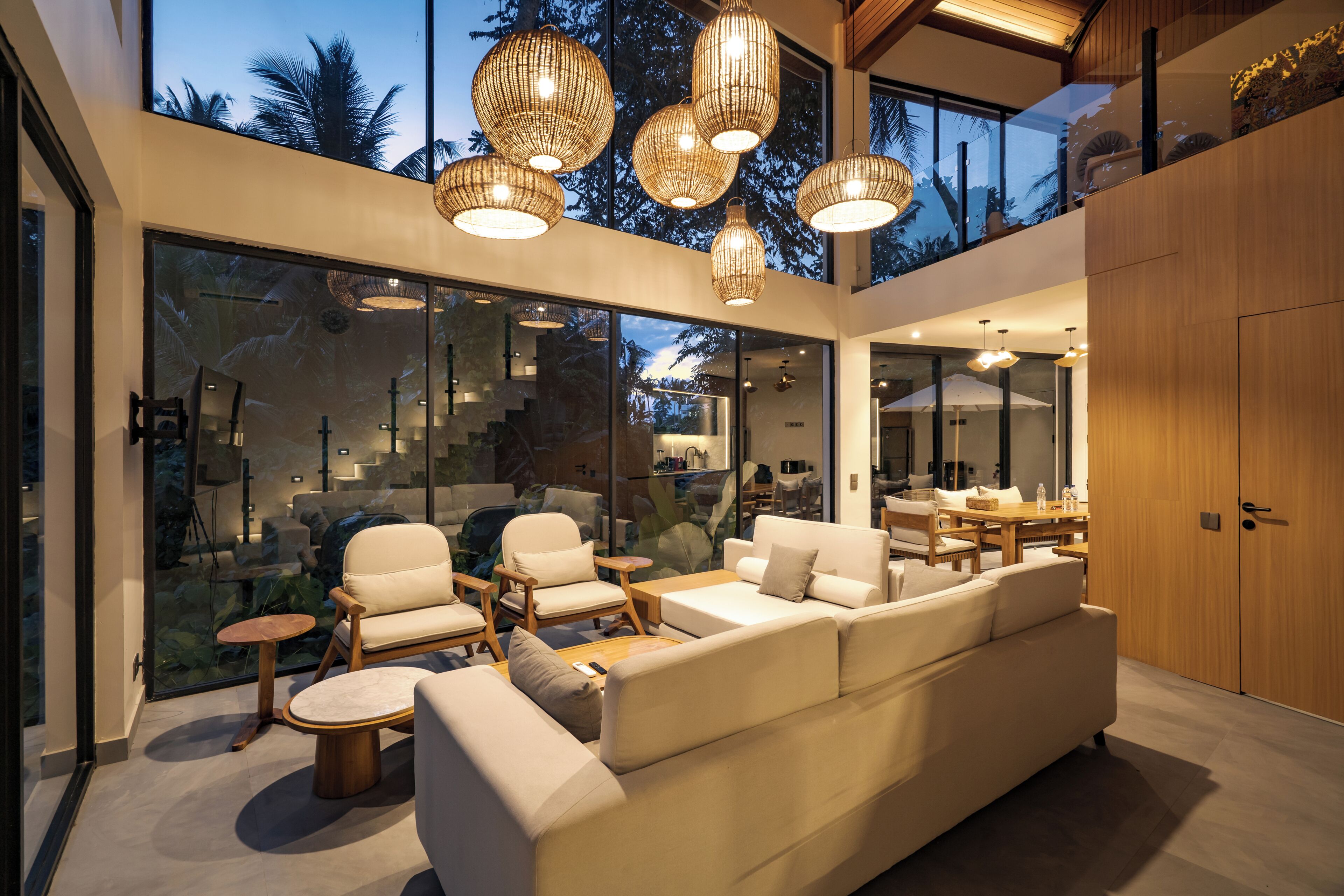 Un interior moderno con un sofá, sillas y zona de comedor, amplias puertas de cristal y vistas a árboles.