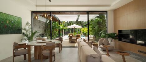 A modern living room with a dining area, a large TV, and a view of a pool and garden.