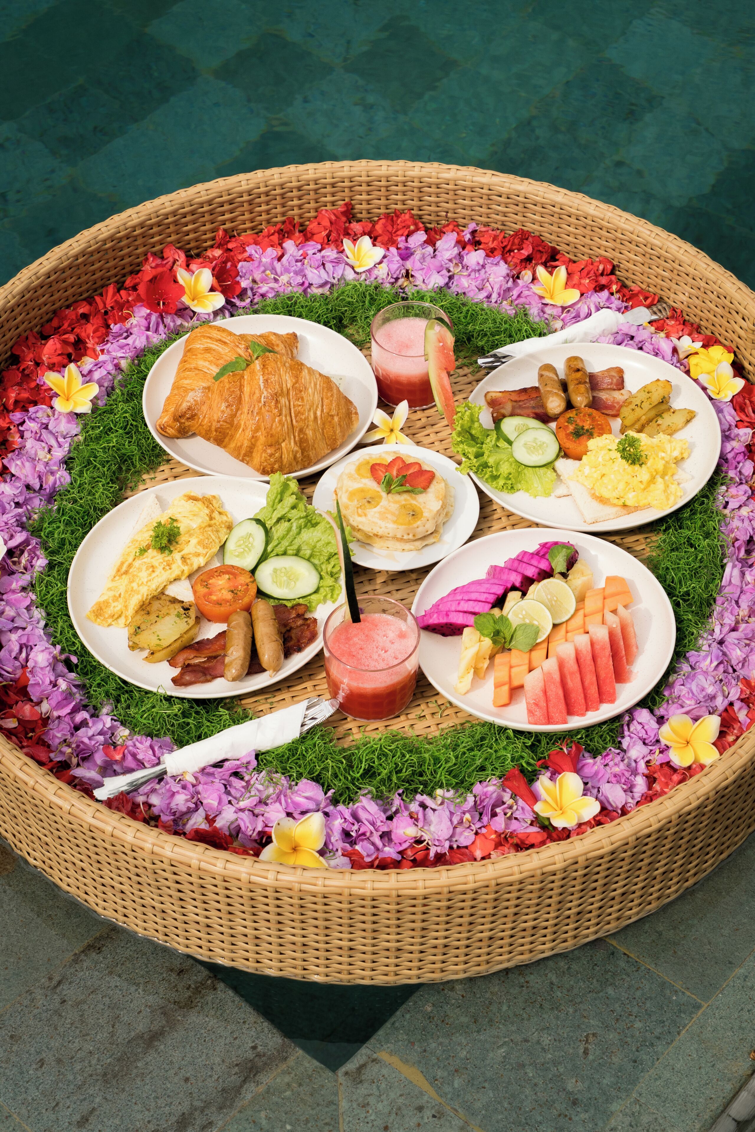 A round wicker table with various breakfast items and flowers.
