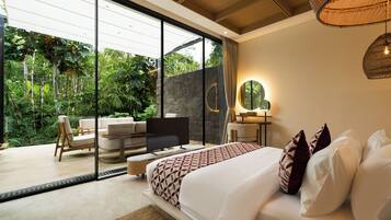 A bedroom with a large bed, a television, a sofa, and a dining area with a view of lush greenery.