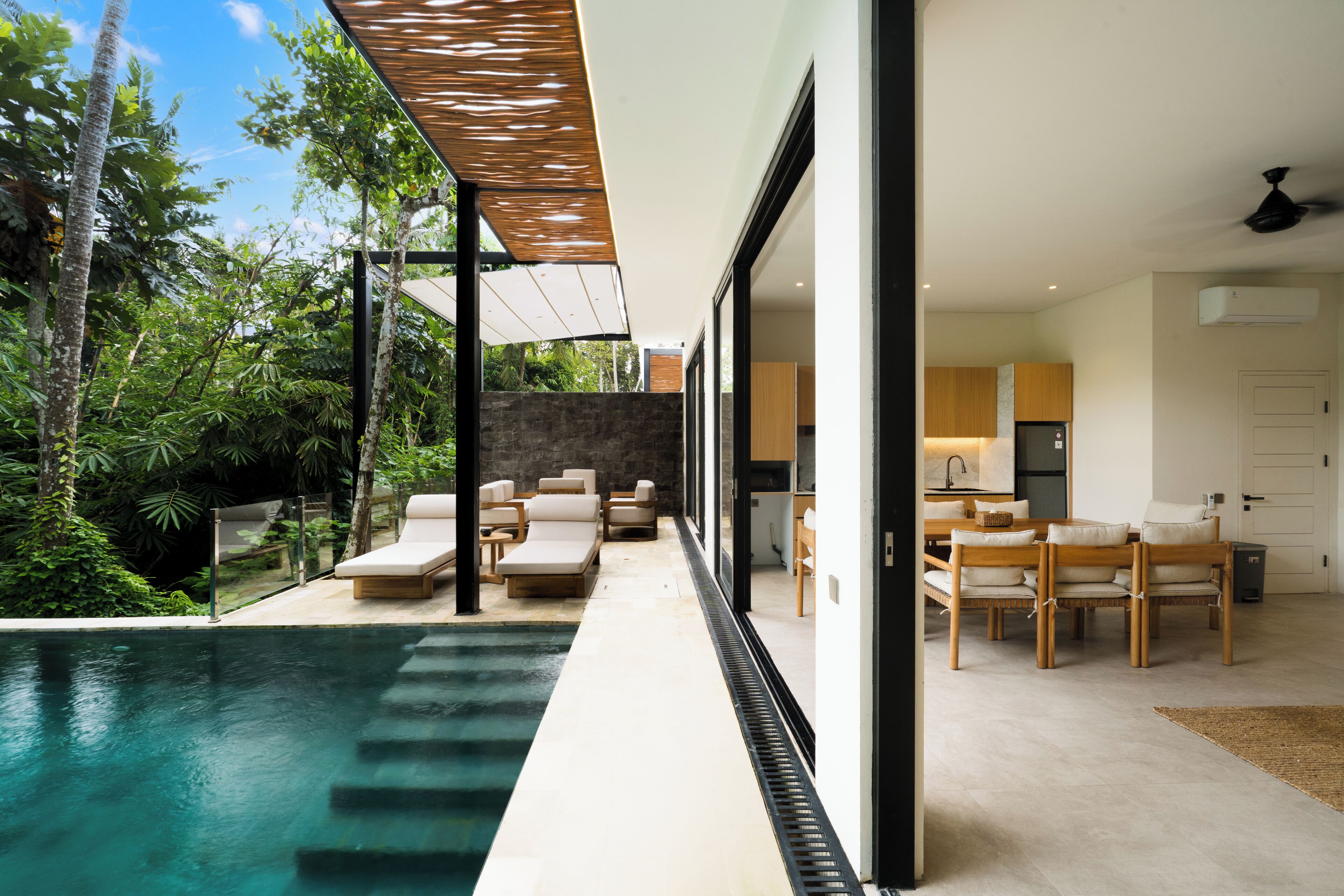 A modern house with a swimming pool, outdoor seating, and a kitchen visible through large windows.