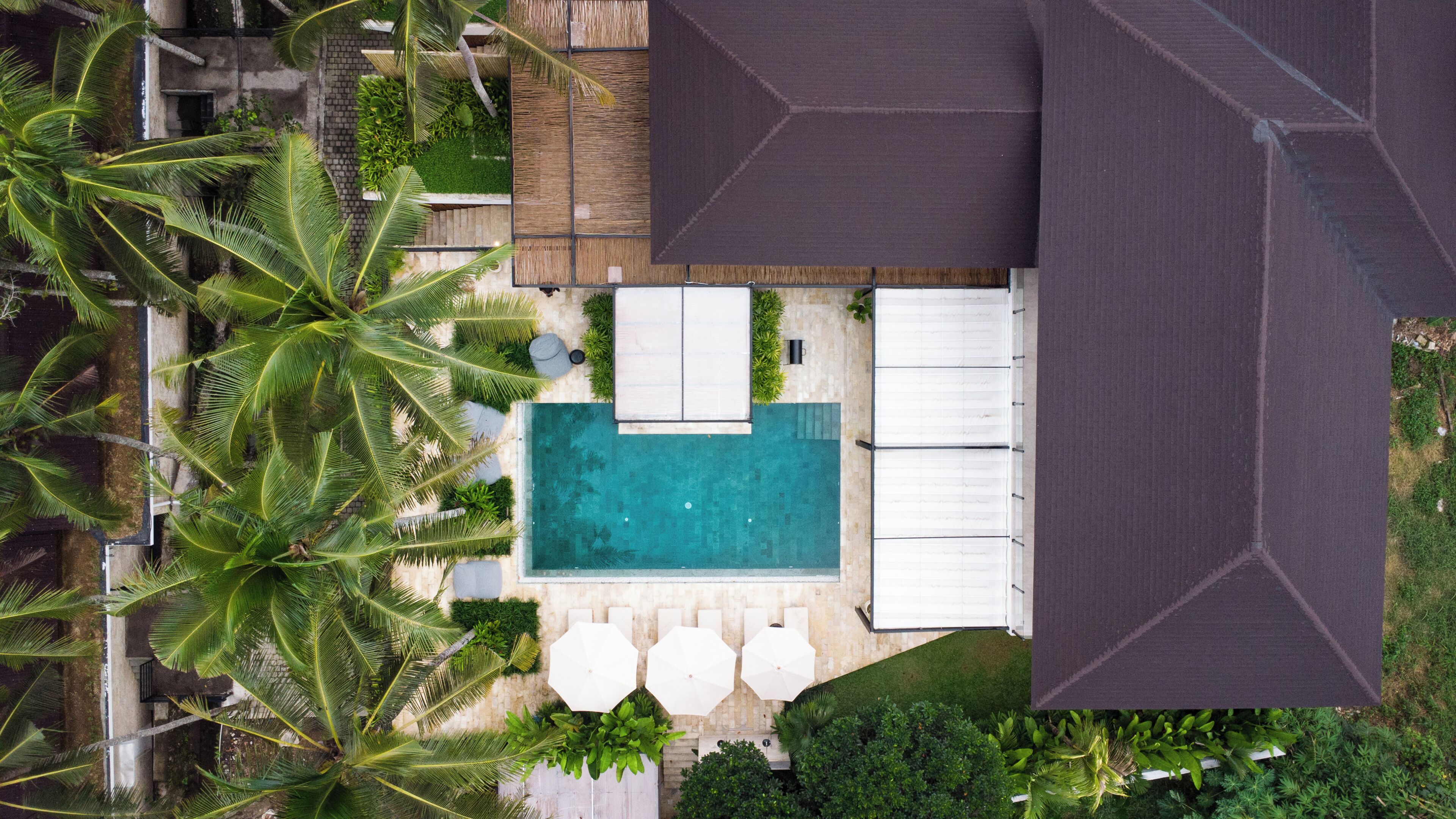 Vue aérienne d’un complexe hôtelier avec une piscine, des chaises longues et des palmiers.