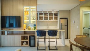 A modern kitchen with a built-in TV, a refrigerator, and a bar area with stools.