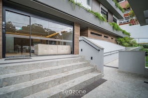 A modern building with a glass facade, outdoor seating area, and a staircase leading to a terrace. - Apt w/ BBQ & Balcony 220 m From the Beach Rty0216 (Florianópolis)