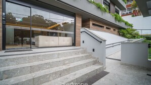 A modern building with a glass facade, outdoor seating area, and a staircase leading to a terrace.