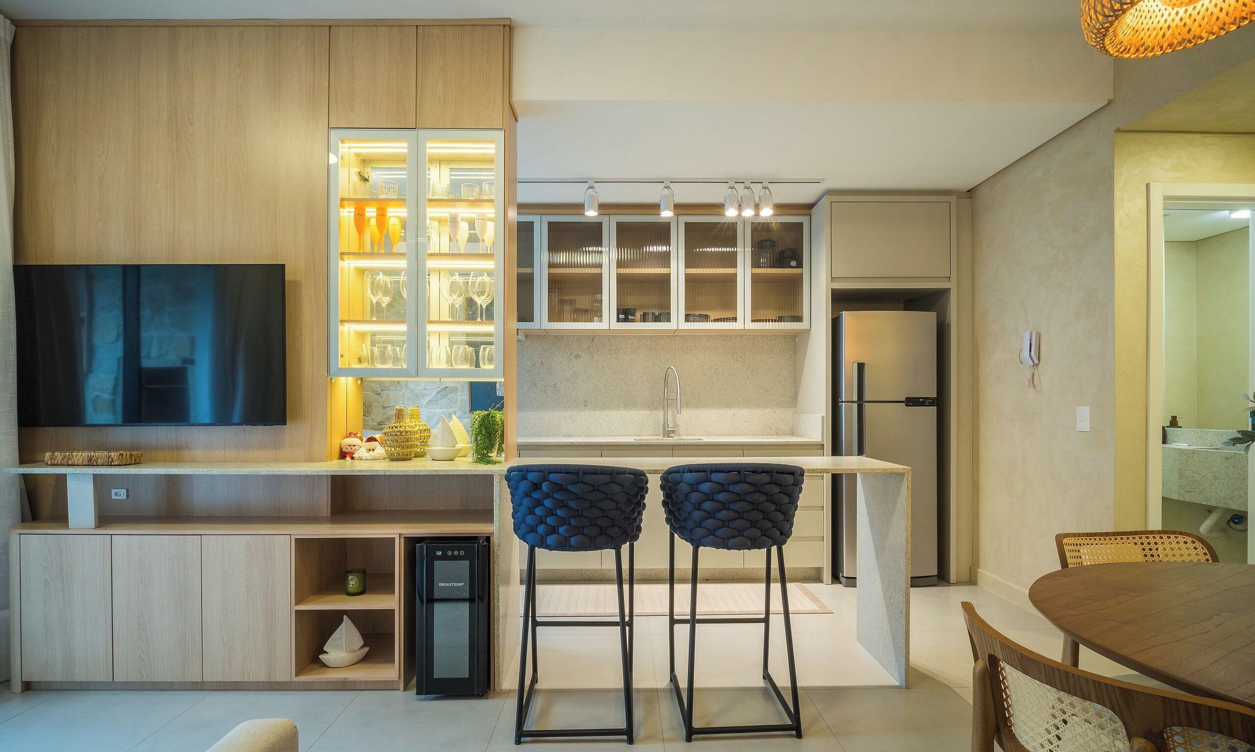 A modern kitchen with a built-in TV, bar stools, and a refrigerator.