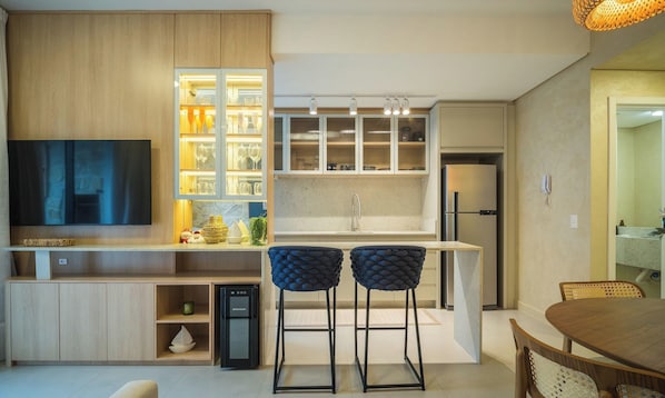 A modern kitchen with a built-in TV, bar stools, and a refrigerator. - Apt w/ BBQ & Balcony 220 m From the Beach Rty0216 (Florianópolis)