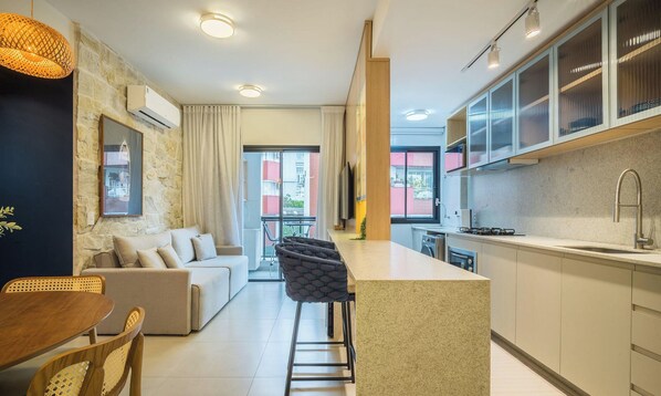 Una cocina moderna con una isla central, un comedor con sofá y sillas, y vistas al exterior a través de un ventanal.