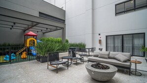 A modern outdoor patio area with a children's play structure, seating arrangements, and a fire pit.