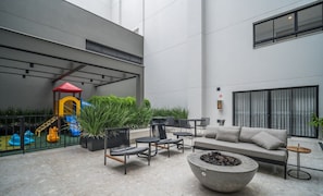 Un patio exterior moderno con juegos infantiles, zonas de estar y un hogar para la chimenea.