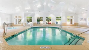 Una piscina interior con agua cristalina, un trampolín y un cartel de socorrista.