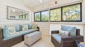 Una habitación con un ventanal grande, muebles de mimbre, un ventilador de techo y un espejo.