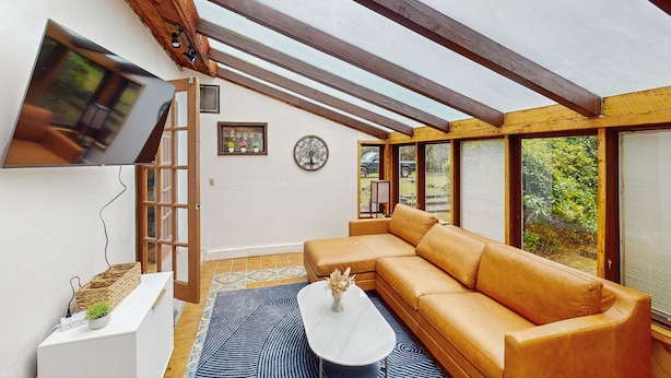 A modern living room with a large sectional sofa, a flat-screen TV mounted on the wall, and a wooden ceiling structure. - Charming house w/ wifi, fireplace & dog-friendly (Shelton)