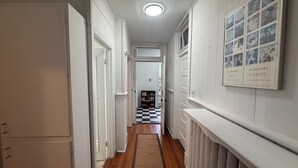 Un couloir aux murs blancs, avec un sol à carreaux et un radiateur sur le côté droit.